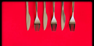 Farsi aiutare in casa dai figli: si può riuscire? Posate su sfondo rosso: apparecchiare la tavola come primo passo per farsi aiutare in casa dai figli